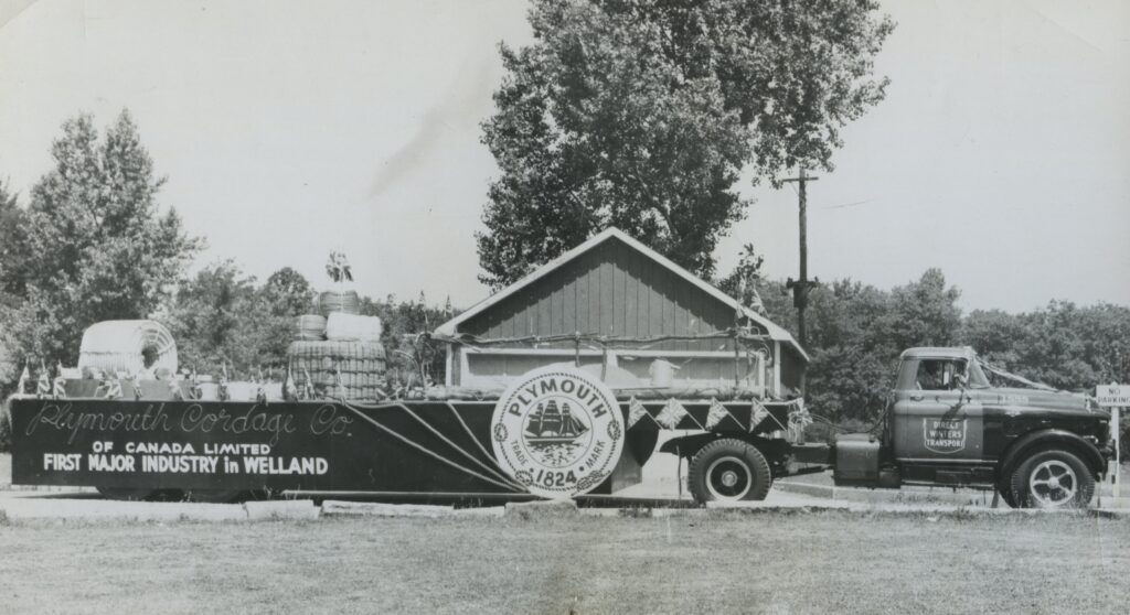 A parade float  with rope and twine is pulled by a truck. On the side is painted "Plymouth Cordage Co. of Canada limited first major industry in Welland, Plymouth 1824."