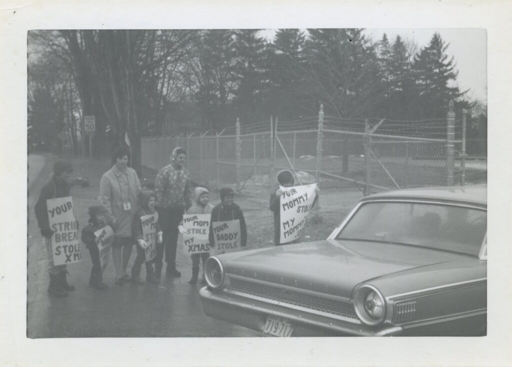 An old photograph showing two adults and several children holding signs while a car passes by.
