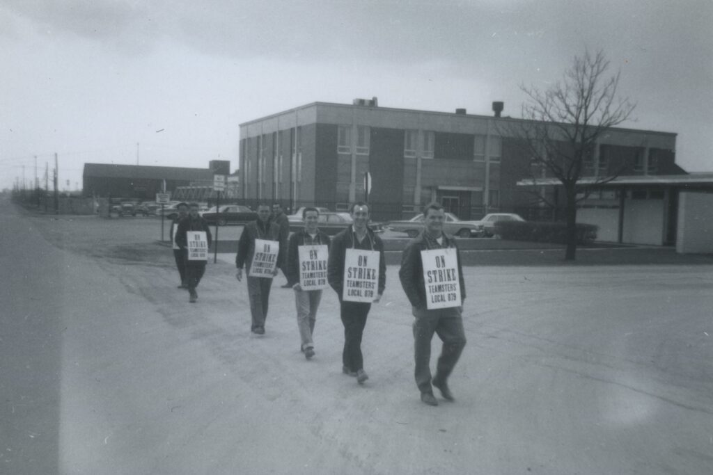 Several men walk in a row, each wearing a sign on his chest. 