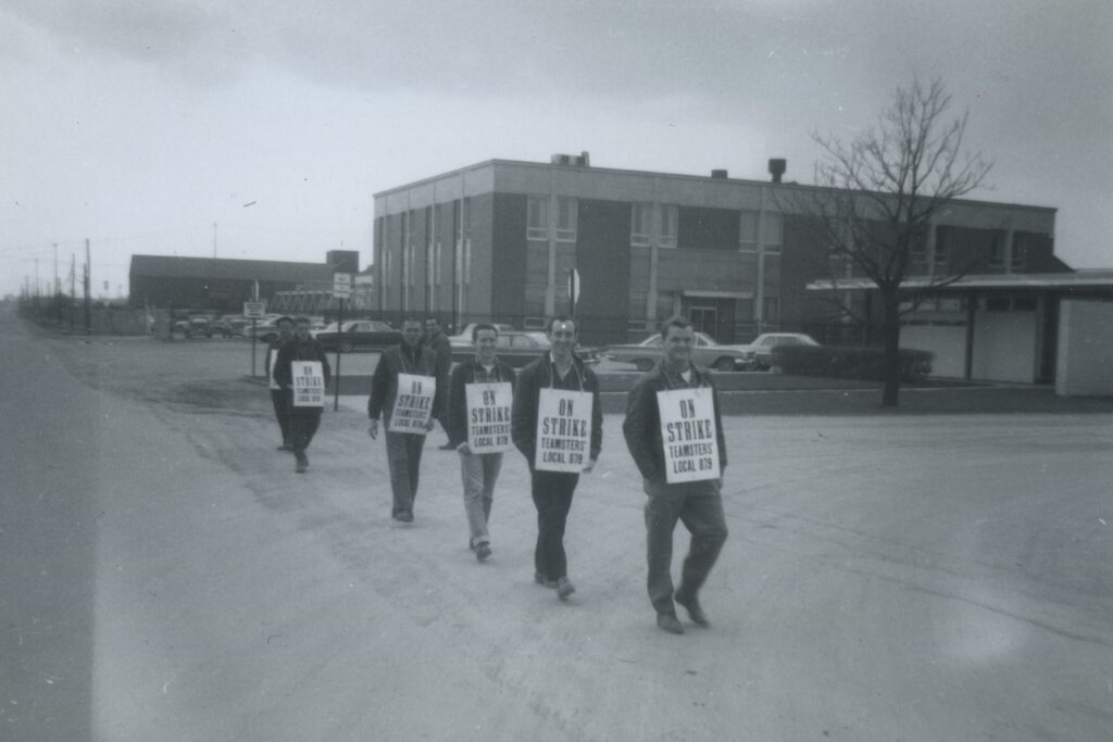 Men walk in a line, each with a sign on his torso.