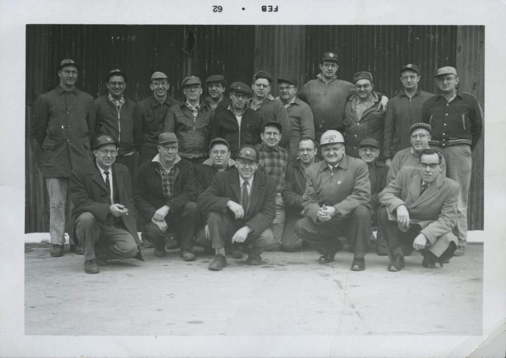 Two rows of men pose for a photo. The back row stands, and the front row crouches.