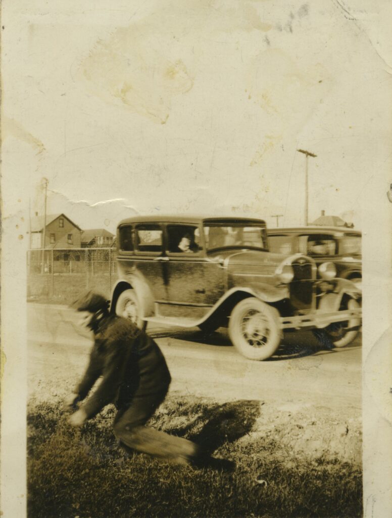 An old photo of a vehicle, with a man in the foreground.